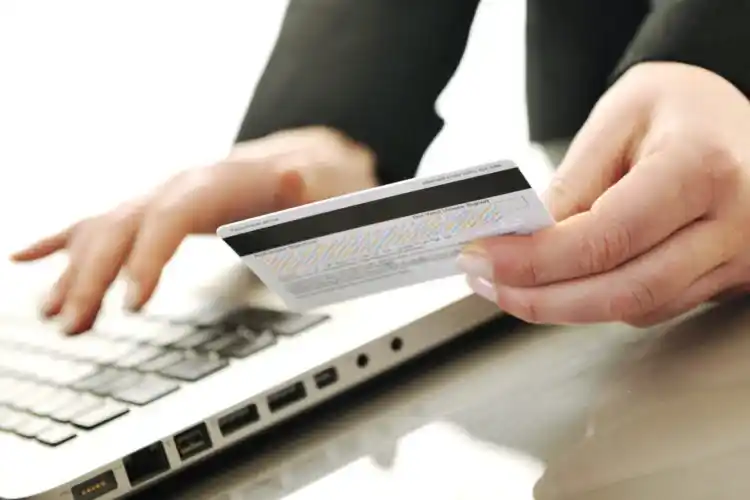 Person holding a bank card while entering details on a laptop.